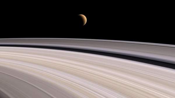 Una falce di Titano si staglia in lontananza sulla sottile struttura degli anelli di Saturno 